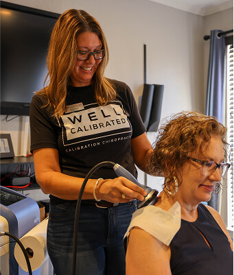Chiropractic assistant using laser therapy device on female patient’s shoulder.