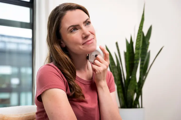 Woman using handheld device on neck while smiling thoughtfully.